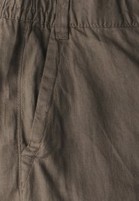 Brun vävd textil på nära håll med en avslappnad midja, sidofickor och subtil textur med synliga söm detaljer.