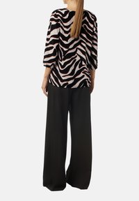 Schwarz-beige Zebra-Print-Oberteil mit Dreiviertelärmeln, kombiniert mit locker sitzenden schwarzen Hosen. Weicher Stoff, entspannte Gestaltung.