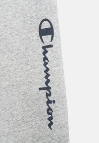 Harmaa puuvillakangas, jossa on harjattu pinta, ja tummansinisellä "Champion"-logolla kursiivilla sivussa. Yksinkertainen ja siisti suunnittelu.