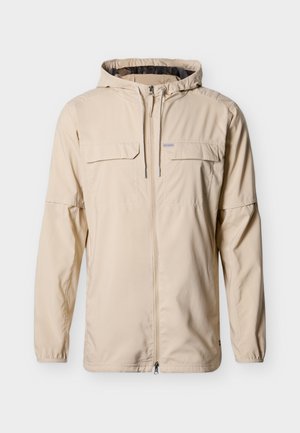 Bež jakna s kapuco, sprednjo zadrgo, vrvico za zategovanje, dvema žepoma na prsih s poklopcema in elastičnimi manšetami, prikazana na belem ozadju.