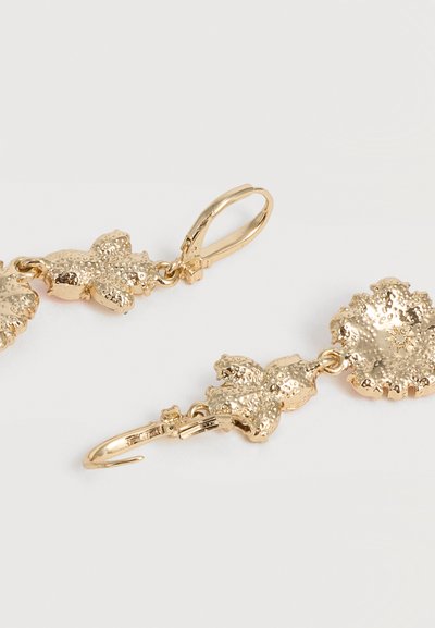 Σκουλαρίκια κρεμαστά με χρυσή απόχρωση, υφασμένα, ακανόνιστου σχήματος φύλλα και κούμπωμα με αντενεργό κλείδωμα σε απλό λευκό φόντο.