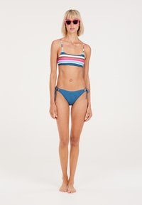 Bikini komplektas su daugiaspalviu raištiniu viršumi su plonais petnešėlėmis ir vienspalvėmis mėlynomis kelnaitėmis su rišamomis šoninėmis juostomis. Švelni audinio tekstūra.