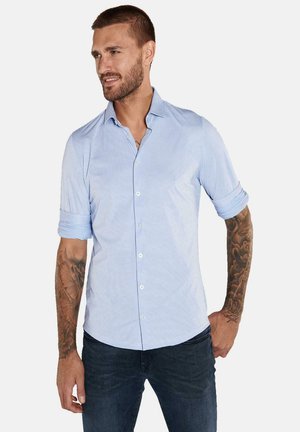 Hellblaues Hemd mit Karomuster, hochgekrempelten Ärmeln und klassischem Kragen. Getragen mit dunkelblauen Jeans. Baumwollmischmaterial.