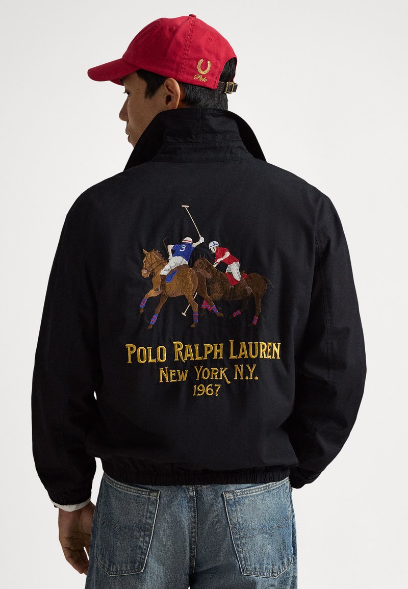 Veste noire avec scène de polo brodée en couleurs représentant des chevaux et des cavaliers. Texte doré indiquant "Polo Ralph Lauren New York N.Y. 1967."
