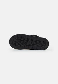 Schwarze Sneakersohle aus Gummi. Verfügt über ein strukturiertes Profil für besseren Grip und enthält das Markenlogo, das auf der Oberfläche eingeprägt ist.