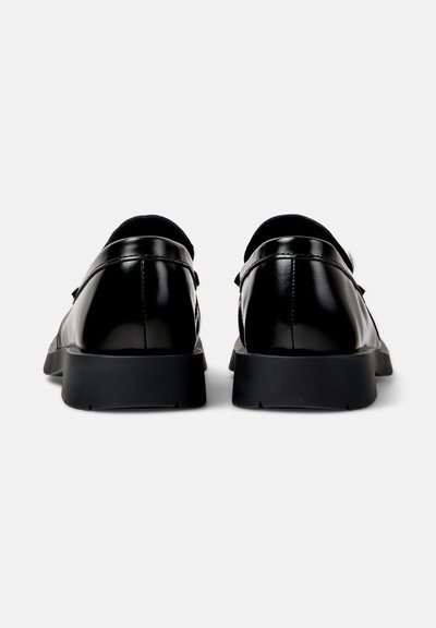 Pair of shiny black leather loafers viewed from the back, with thick black soles on a white background.