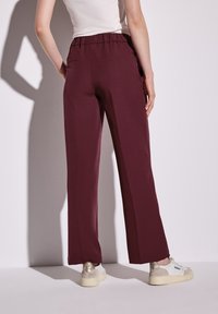 Pantalons larges bourgogne avec une taille élastique, des poches latérales et une texture lisse, associés à des baskets blanches et un haut ajusté.
