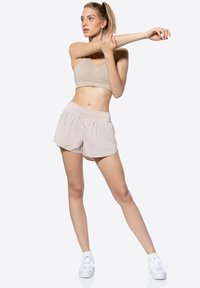 Reggiseno sportivo beige chiaro e pantaloni corti abbinati con vita elastica, tessuto liscio e vestibilità comoda, abbinati a scarpe da ginnastica bianche.