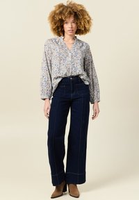 Blusa floreale a maniche lunghe con collo volan, dotata di una fila di bottoni, abbinata a jeans scuri a vita alta e gamba larga con cuciture a contrasto.