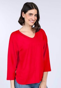 Rotes, V-förmiges Oberteil aus weichem Stoff mit Dreiviertelärmlen und lockerer Passform, ausgestattet mit einem abgerundeten Saum und minimalen Nähdetails.