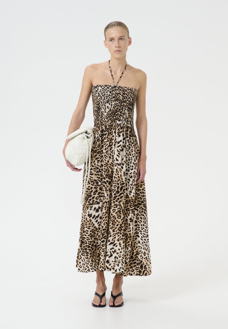 Maxikjole med leopardprint og uden stropper, lavet af letvægtsstof. Modellen holder en hvid quiltet taske og har sorte flip-flops på.