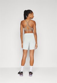 Sports bra in light brown with crisscross straps and an open back, paired with mint green high-waisted shorts. Black sneakers with pink accents.