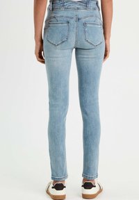 Jean skinny bleu clair avec des accents cousus et deux poches arrière, associé à des baskets blanches avec un capuchon noir.