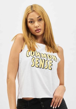 Hvit avkortet tanktop med fed bold svart og gul tekst som sier "COMMON SENSE." Stoffet ser mykt ut; designet er enkelt og avslappet.