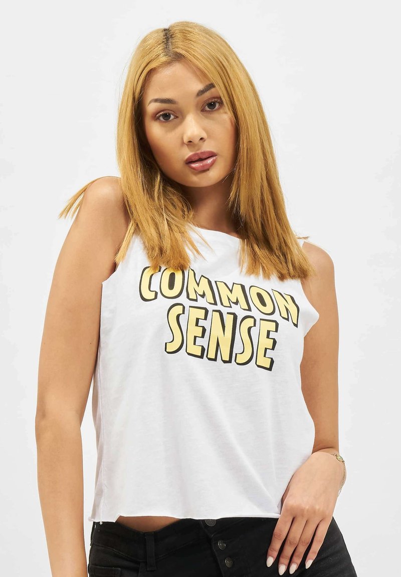 Hvit avkortet tanktop med fed bold svart og gul tekst som sier "COMMON SENSE." Stoffet ser mykt ut; designet er enkelt og avslappet.