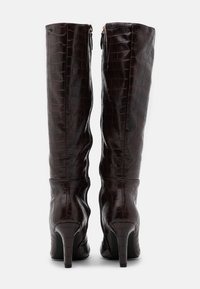 Bottes hautes en cuir embossé crocodile brun avec un design ajusté, texture lisse et talons aiguilles, dotées de fermetures éclair latérales.