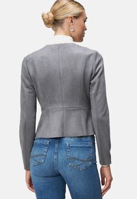 Giacca in suede grigio con un design aderente, spalle arrotondate e dettagli sulle cuciture, abbinata a jeans in denim blu con tasche posteriori.