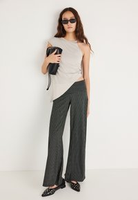 Asymetryczna beżowa bluzka z zakręcanym detalem, zestawiona z czarnymi, szerokimi spodniami w paski. Do tego czarna torebka i spiczaste baleriny.