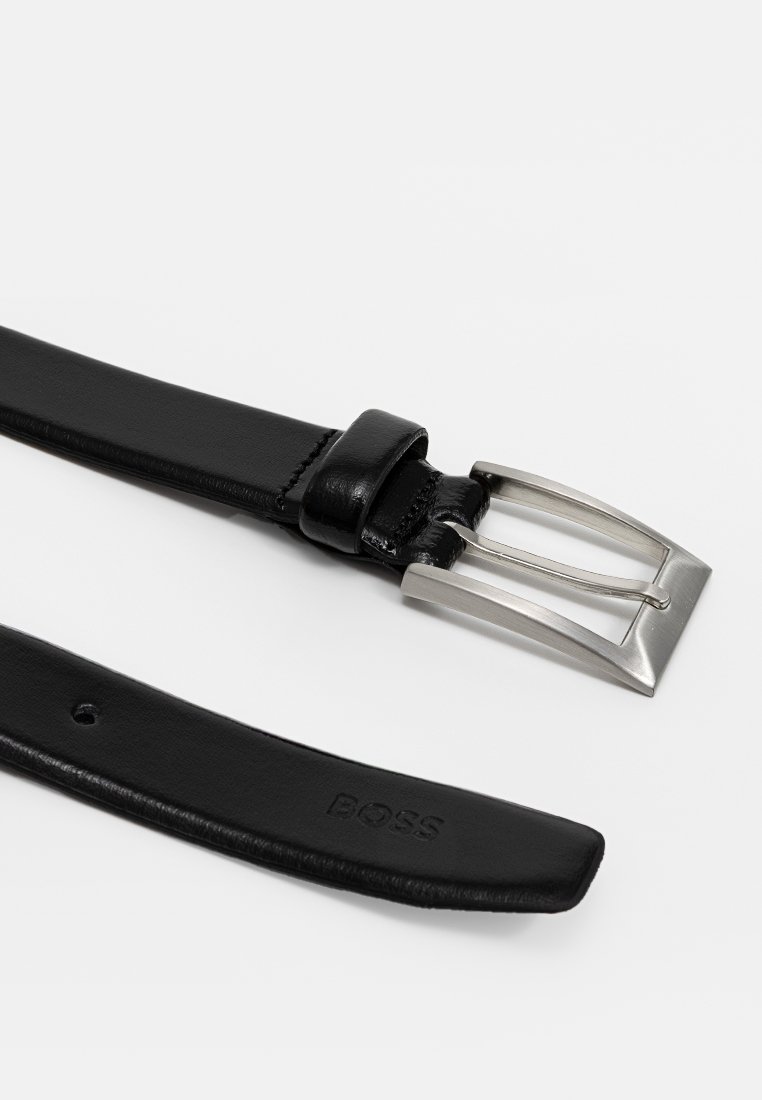 Cinturón de cuero negro con textura suave, hebilla rectangular de metal plateado y un detalle de marca grabado en la correa.