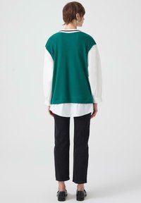 Camicia sovrapposta a costine verde acqua indossata sopra una camicia bianca, abbinata a jeans neri a gamba dritta. Presenta un colletto classico e una vestibilità comoda.