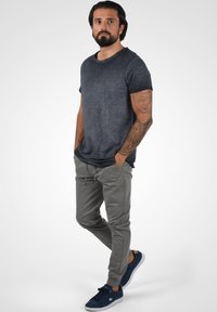Dark gray short-sleeve t-shirt, light gray jogger pants, navy sneakers. Casual fit, soft texture, standing pose with hands in pockets.