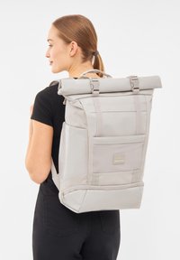 Hengeres hátizsák világosszürke szövettel, párnázott pántokkal, elülső hálós zsebbel és logóval. Simább textúra, tartós kialakítás és állítható záródások.