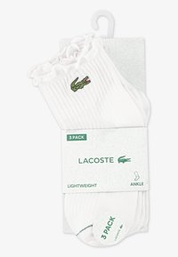 Λευκές ασπρόμαυρες κάλτσες αστραγάλου με ριγέ υφή, σε συσκευασία τριών τεμαχίων, με πράσινο λογότυπο κροκοδείλου Lacoste στο πλαϊνό μέρος. Ελαφριές με βελούδινο ριγέ άκρο.