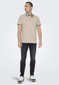 Camisa polo beige con un cuello en blanco y negro, combinada con vaqueros oscuros y zapatillas en blanco y negro. Diseño simple; textura de tela suave.
