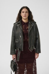 Μαύρο δερμάτινο μπουφάν μοτοσικλέτας με φθαρμένη επιφάνεια, ασημένια μεταλλικά στοιχεία και πολλές τσέπες. Φοριέται πάνω από μια μπορντό δαντελένια φορε�σιά, κρατημένο με μια μαύρη τσάντα.