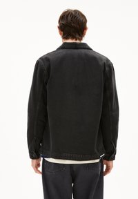 Schwarze Jeansjacke mit Kragen, sichtbaren Nähten und Knopfakzenten. Sie hat eine lockere Passform und ein leicht verkürztes Design.