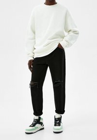 Bílá mikina, černé džíny s opotřebovaným vzhledem a černé vysoké tenisky se světlounce zelenými detaily. Oblečení má volný střih s viditelnými roztrženými koleny.