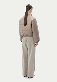 Brun puffjacka med hög krage, elastisk midja och vadderad design, i kombination med beige vida byxor. Strukturerad tyg.