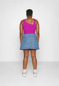 Top roxo sem mangas combinado com uma saia de ganga azul com dois bolsos traseiros, etiqueta na faixa da cintura e ténis brancos com pormenores em cinza.