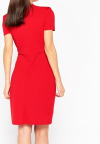 Rotes, tailliertes Kleid mit kurzen Ärmeln, das Schulterfalten und einen nahtlosen Rücken aufweist. Glatte Stofftextur, knielanger Schnitt.