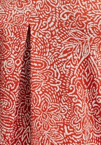 Tejido rojo con un patrón floral blanco en espiral, que presenta detalles y texturas intrincados, exhibiendo un material suave y ligero.