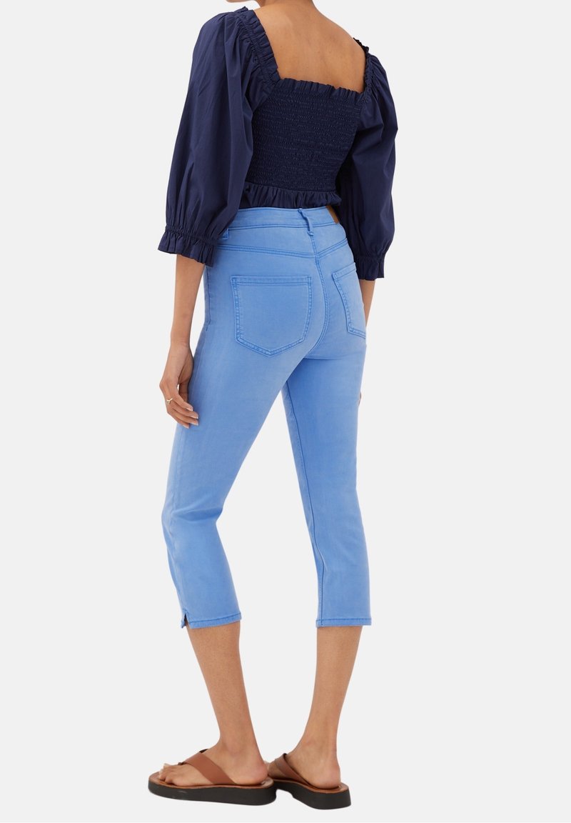 Jeans cortos de color azul claro con un diseño ajustado y bolsillos traseros, combinados con un top navy con fruncido y mangas abullonadas.