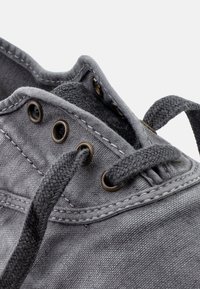 Szürke vászoncipő kerek fém fűzőlyukakkal, lapos textilfűzőkkel és texturált felsőrésszel. Látható varrás és puha bélés részlet.