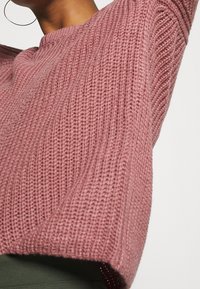 Gebreide trui in zacht roze, met een geribbelde textuur en een ronde halslijn. Iets cropped ontwerp met verlaagde schoudernaden.