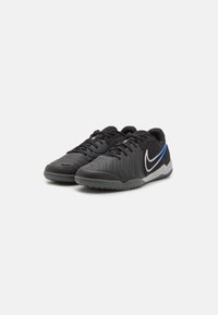 Pár černých sportovních bot s texturovaným svrškem, černými šňůrkami, bílým a modrým logem Swoosh a šedou podrážkou na bílém pozadí.