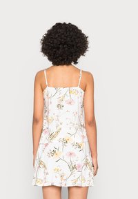 Blommig klänning med tunna axelband, med en vit bakgrund och ett mångsidigt mönster av pastellfärgade blommor, avslappnad passform och en kjol med utsvängd form.