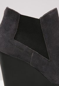 Stivale alla caviglia grigio con tomaia in camoscio e pannello elastico. Tacco a zeppa e suola nera liscia. Design minimalista con un sottile dettaglio di branding.