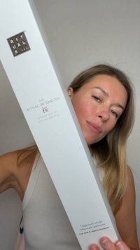 Kvinna som håller en lång vit låda med Ritual of Sakura doftpinnar med risgröt och körsbärsblomssdoft.