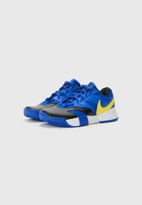 Blue and black athletic shoes with a yellow swoosh, synthetic upper, textured toe, and a white and blue sole with a patterned tread.