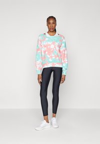 Felpa tie-dye rosa e acquamarina con maniche lunghe, abbinata a leggings neri e sneaker bianche; tessuto morbido e vestibilità comoda.