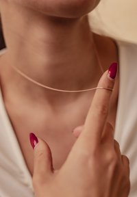 Collier choker en or rose reposant sur la clavicule, maintenu par un doigt. Texture lisse avec un design minimaliste. Court et flexible.