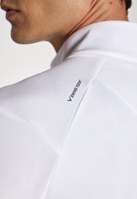 Valge polo särk, millel on sile tekstuur ja kerge sära. Tähtsaks detailiks on "SWING TECH™" logo õlavarre õmblusel.
