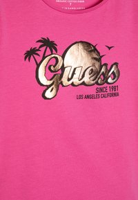 Rosa bomull t-skjorte med et gullmetallisk grafisk trykk med ordet "Guess," palmer, og teksten "Since 1981 Los Angeles California."