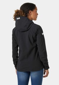 Zwarte softshell jas met een capuchon, voorzien van witte logo-accenten op de achterkant en mouw, en een getailleerd ontwerp voor een gestroomlijnde uitstraling.