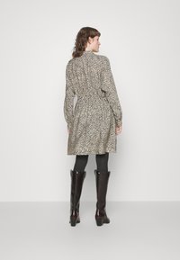 Vestido de estampa de leopardo em tons castanho e creme, com um decote alto, cintura ajustada e saia volumosa. Combinado com meias-calças texturizadas pretas e botas até ao joelho.