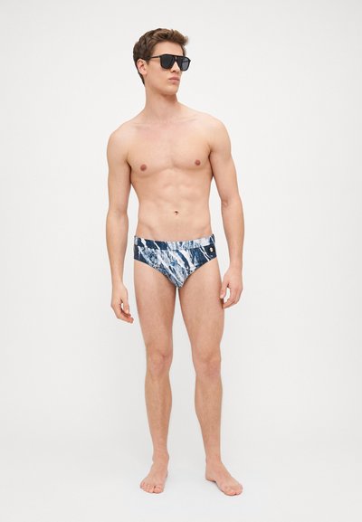 Caleçons de bain en motif marbré bleu marine et blanc, fabriqués en tissu léger. Dotés d'une ceinture contrastante et d'un petit logo sur le côté.